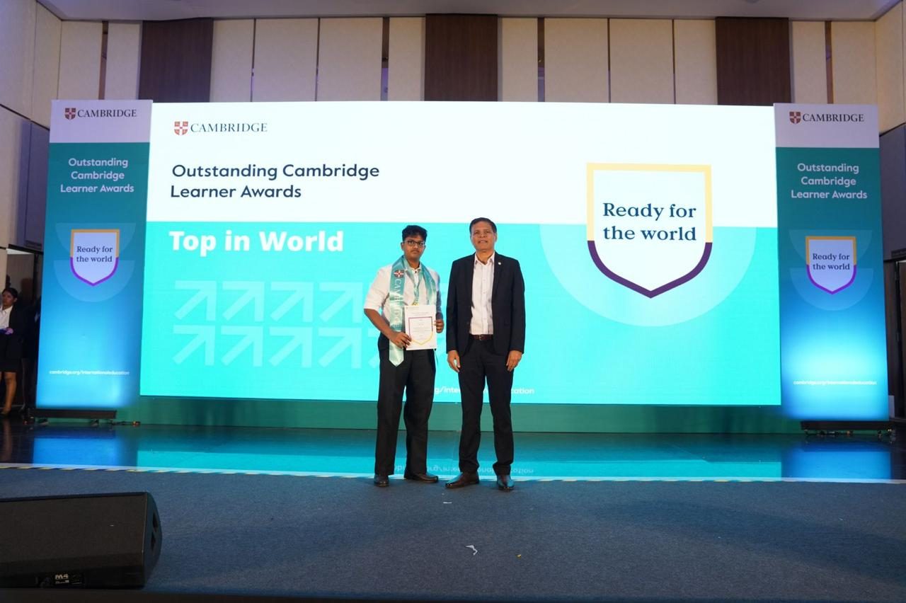 On stage at the Cambridge Outstanding Learner Awards ceremony, standing with the presenter in front of a Top in World backdrop